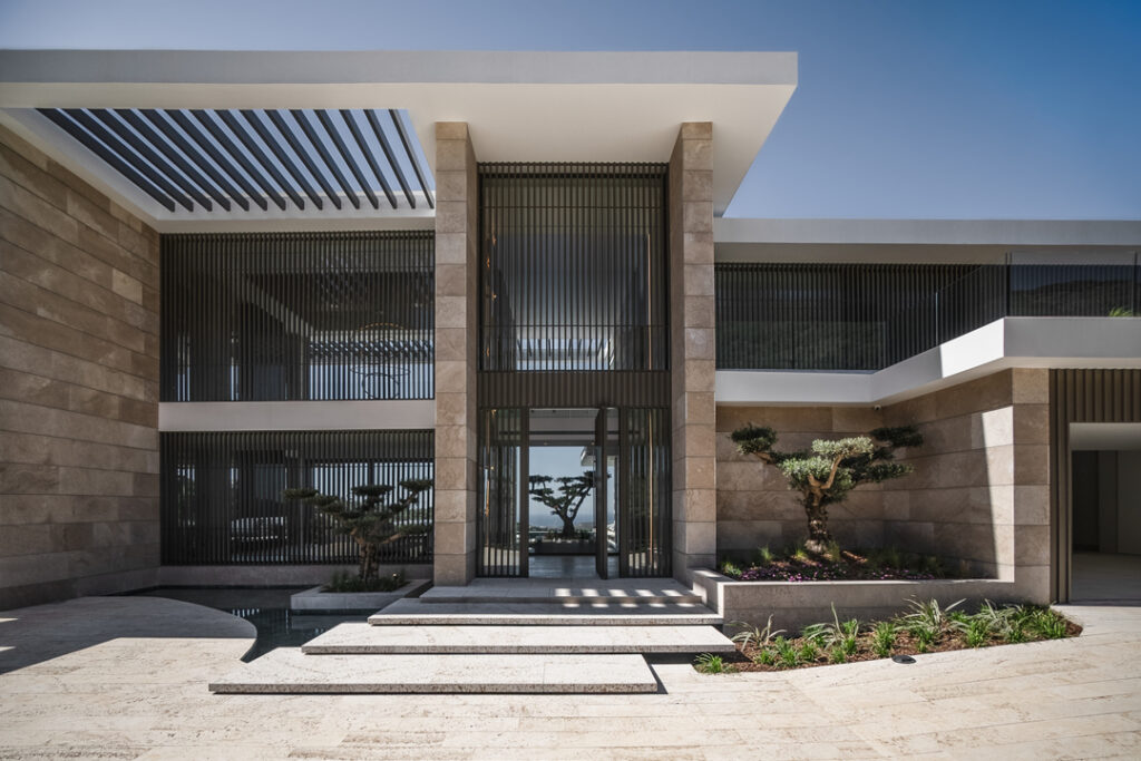 Imposing modern villa entrance with high-ceilings, natural stone cladding and large-scale glass panels in Marbella.