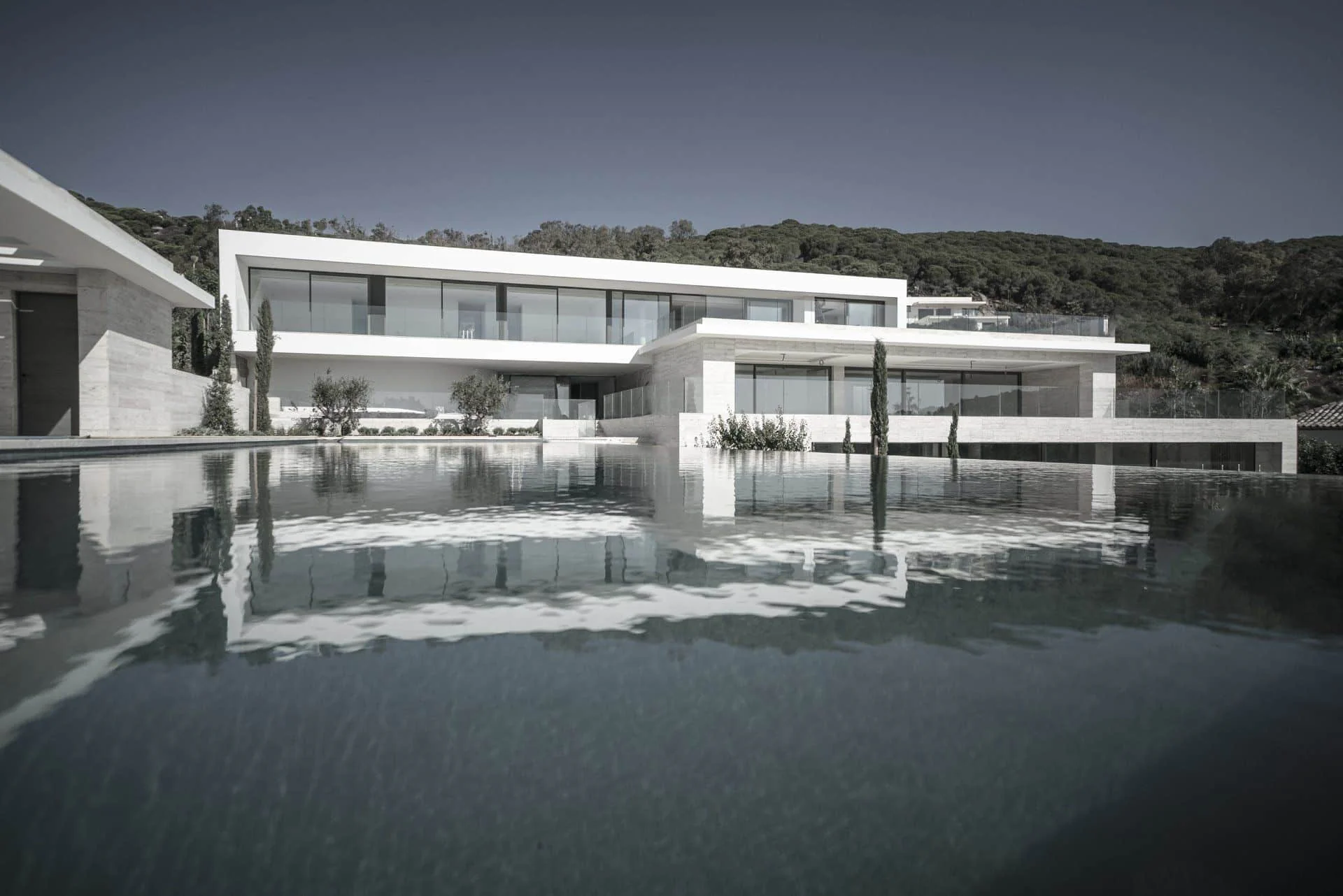 Stunning night perspective of Villa Dorado by ARK Architects with illuminated white volumes reflected in the water.