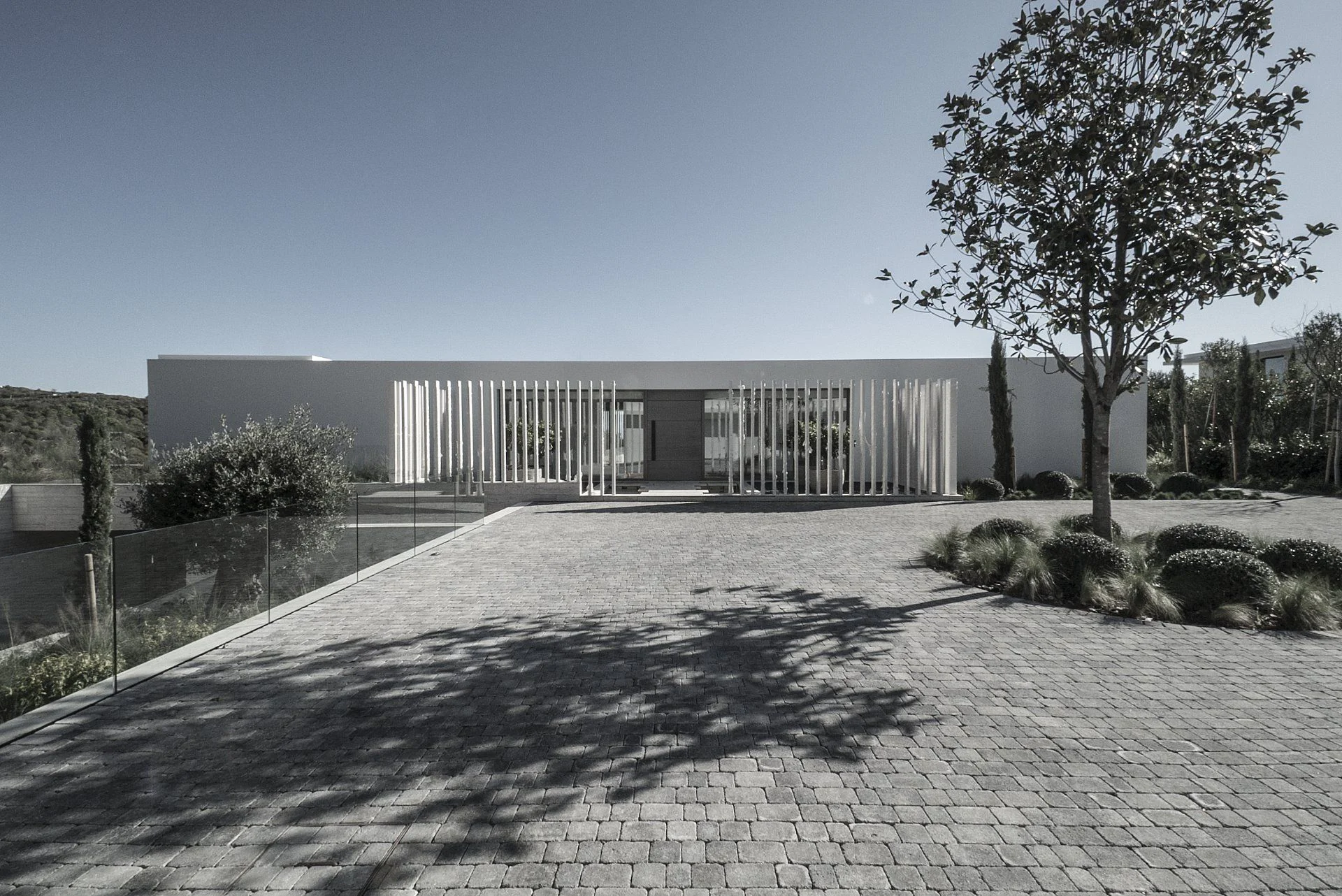 Symmetrical luxury villa entrance featuring a white vertical slat facade and stone-paved driveway.