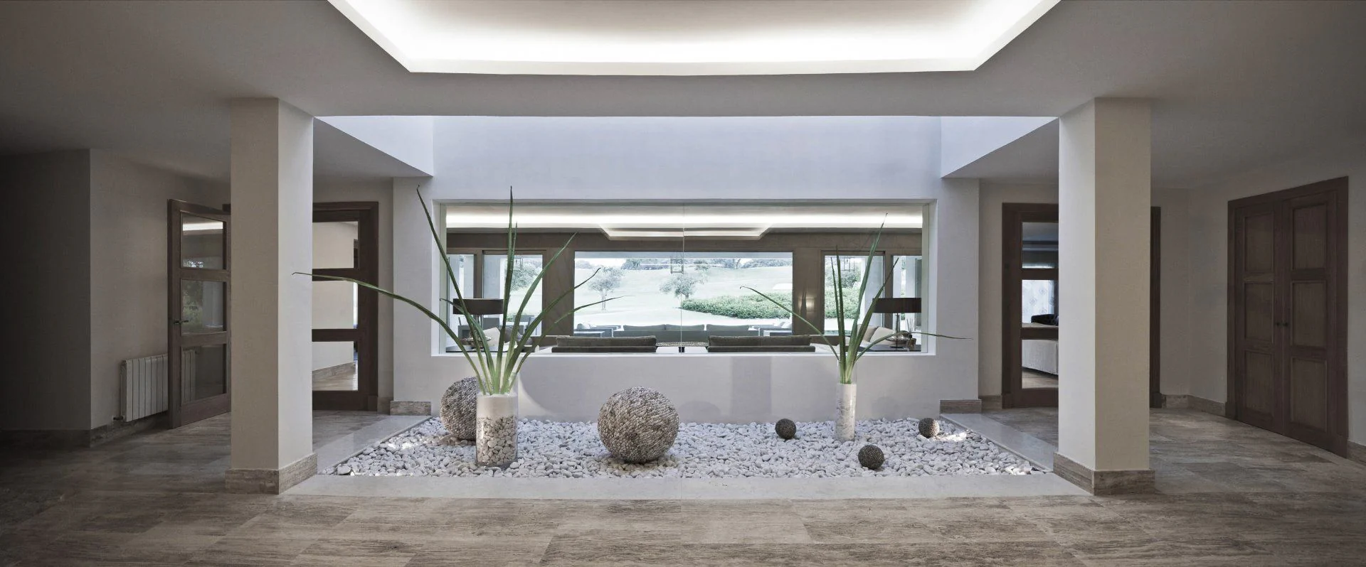 Luxury villa interior featuring a central Zen garden with white pebbles, architectural lighting, and premium travertine floors in San Roque.