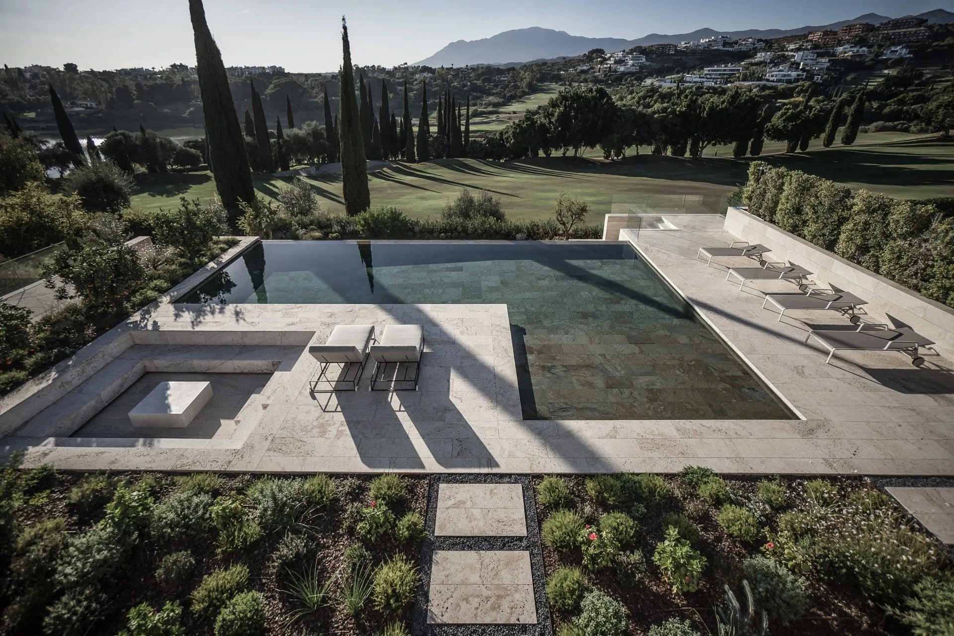 Luxury infinity pool made of natural stone with a built-in sunken fire pit area and panoramic golf views.