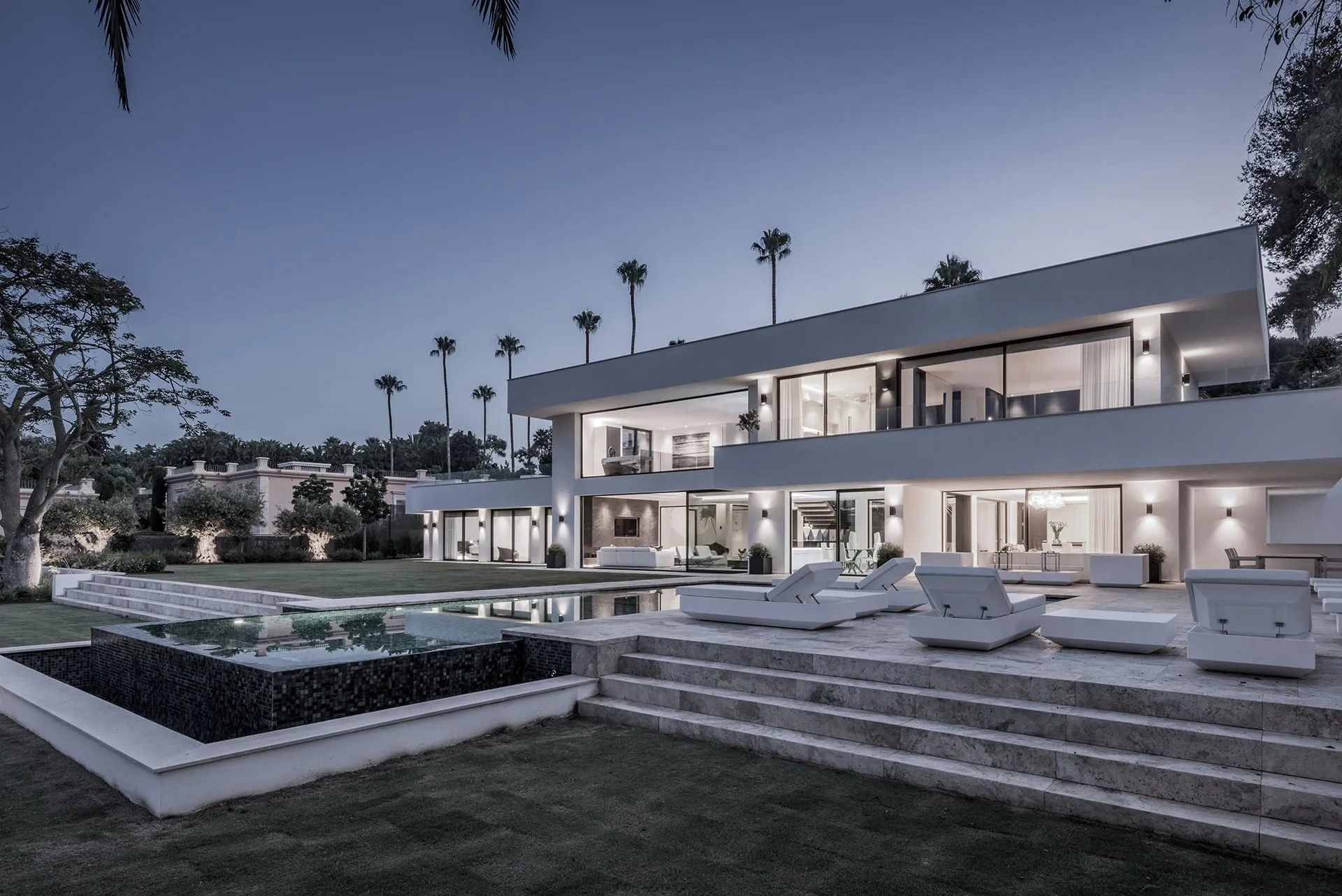 Evening view of a modern villa exterior with strategic architectural lighting and infinity pool by ARK Architects.