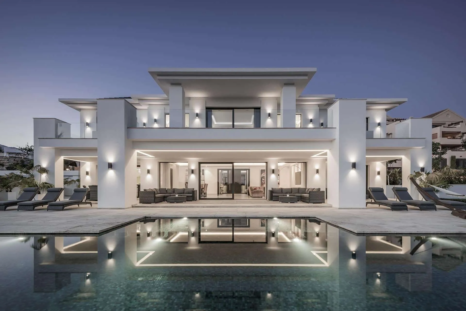 Modern infinity pool with integrated lighting and panoramic coastline views at dusk.