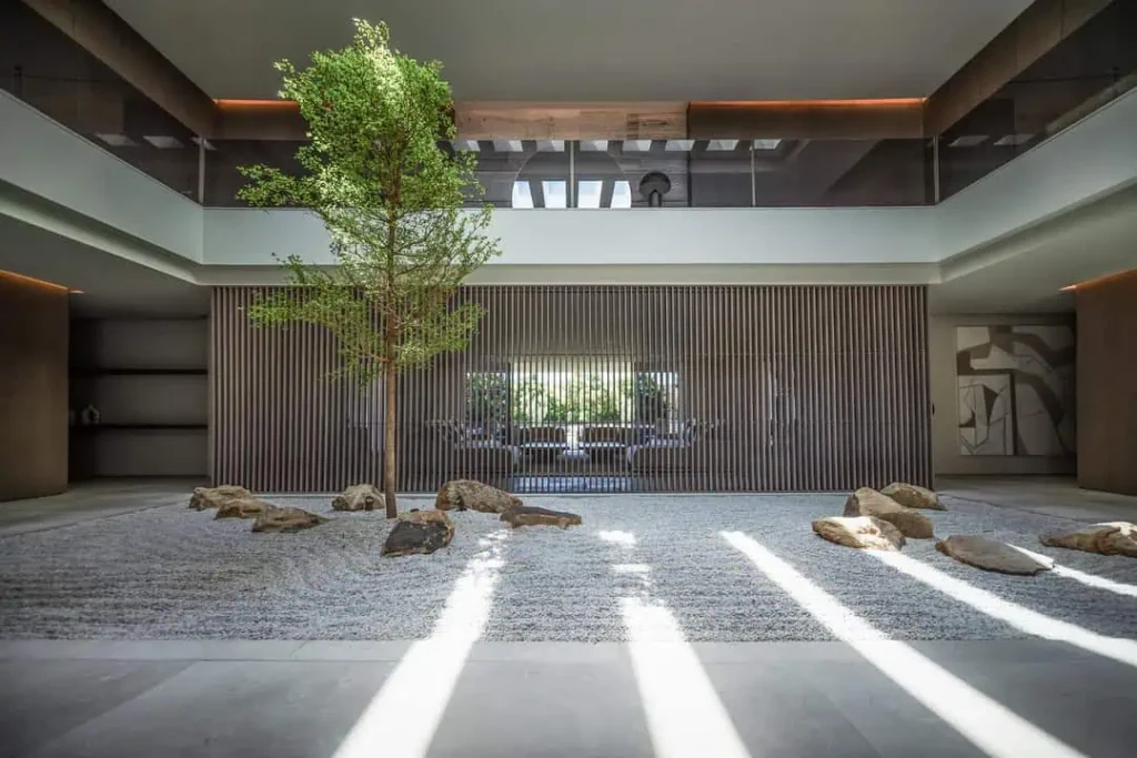 Zen interior courtyard with a central tree, raked gravel garden, and vertical wood slats by Manuel Ruiz Moriche.