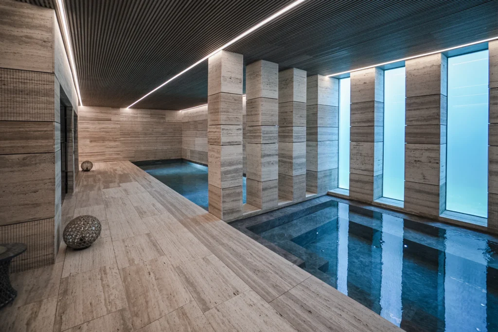 Panoramic view of an indoor pool integrated with the Mediterranean landscape through glass walls.